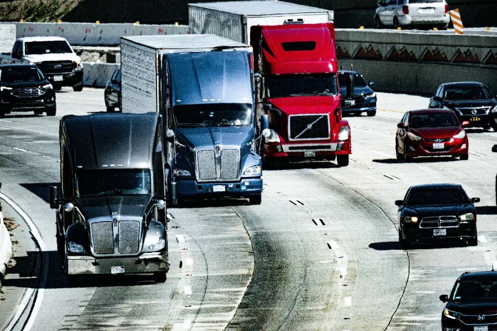 Three shiny trucks travelling down a busy road