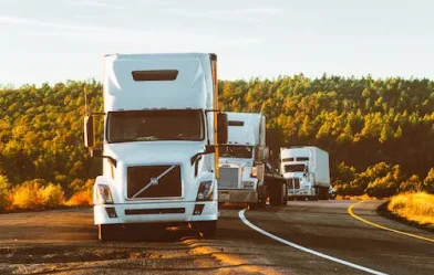 Three white colored commercial trucks parked on the freeway.