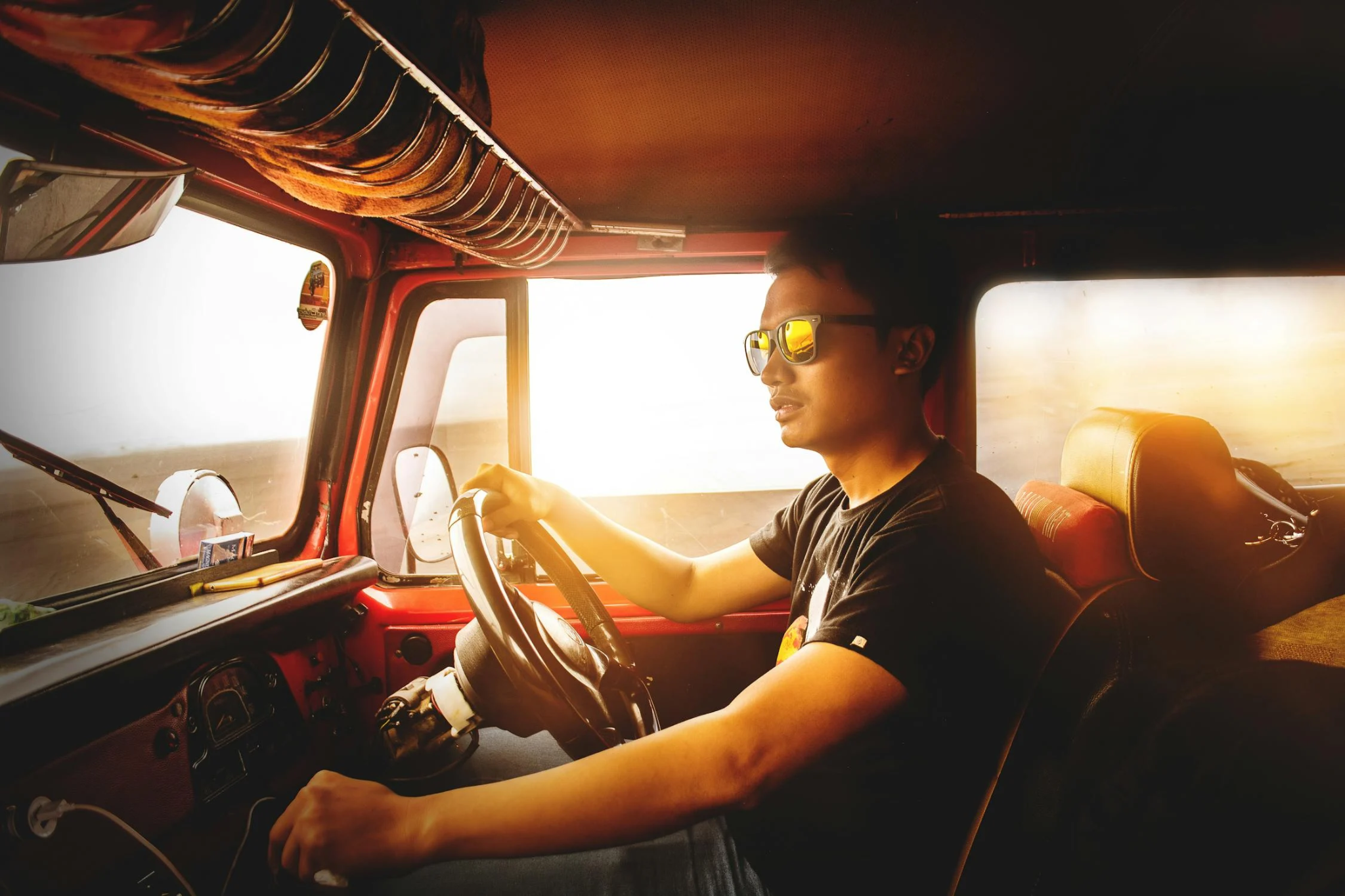 A truck driver wearing sunglasses, driving a truck during sunset.