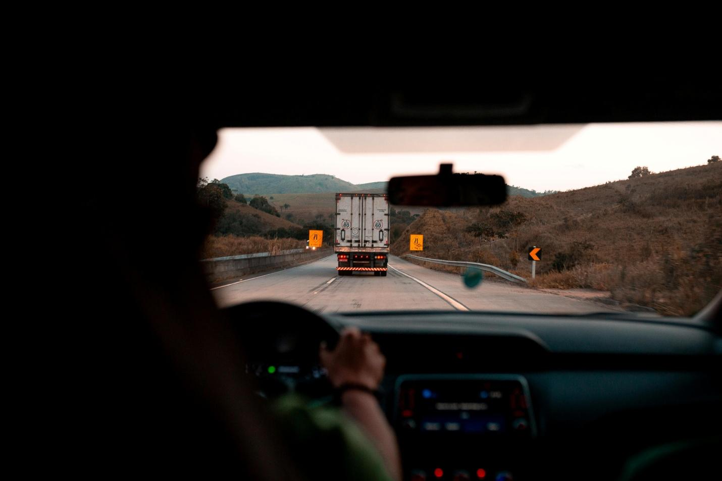 A picture of a view of a truck on the road from the passenger seat of another car