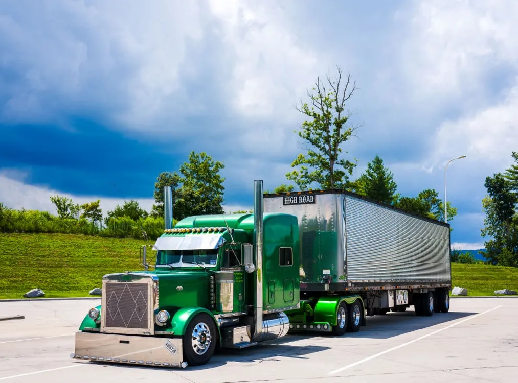 Green truck in front of trees and grass