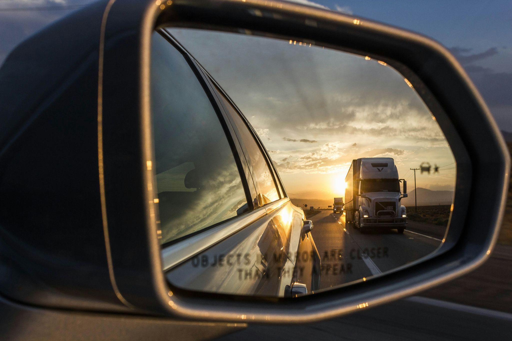 View of a truck driving by through a car’s side mirror